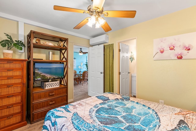 bedroom featuring a wall mounted air conditioner, hardwood / wood-style floors, ceiling fan, and connected bathroom