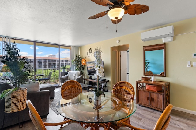 dining area featuring a wall mounted air conditioner, light hardwood / wood-style flooring, floor to ceiling windows, ceiling fan, and a textured ceiling