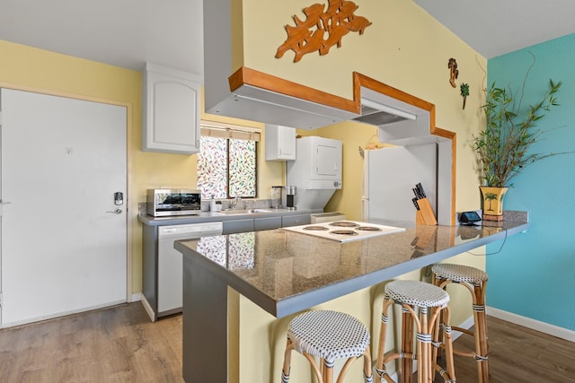 kitchen featuring stacked washer and clothes dryer, light hardwood / wood-style floors, white cabinetry, and white appliances