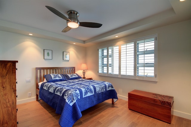 bedroom with ceiling fan, a tray ceiling, and light hardwood / wood-style flooring