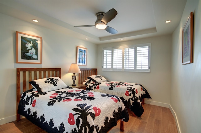 bedroom featuring light hardwood / wood-style floors, ceiling fan, and a tray ceiling