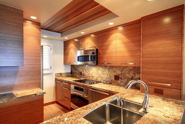 kitchen featuring tasteful backsplash, light stone counters, stainless steel appliances, light hardwood / wood-style floors, and sink