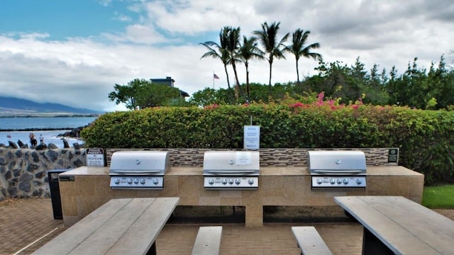 view of patio with exterior kitchen, area for grilling, and a water view