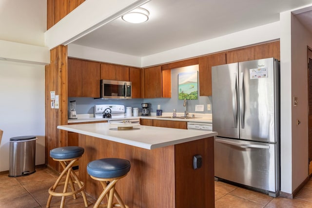 kitchen featuring a kitchen breakfast bar, appliances with stainless steel finishes, sink, and light tile floors