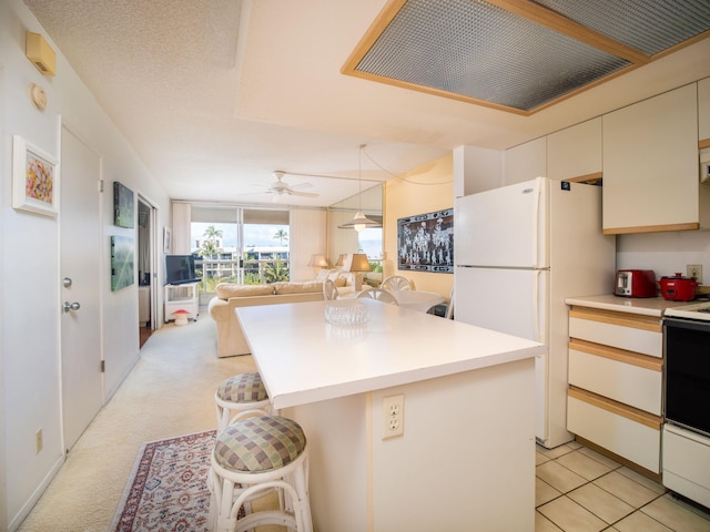 kitchen with ceiling fan, light colored carpet, white appliances, a kitchen bar, and a kitchen island