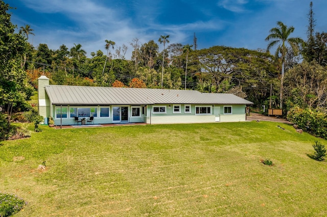 rear view of property with a standing seam roof, a yard, a chimney, and metal roof