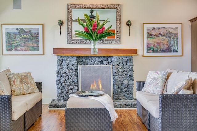 living area with baseboards, visible vents, wood finished floors, and a stone fireplace