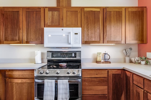 kitchen featuring light countertops, white microwave, brown cabinetry, and stainless steel electric range