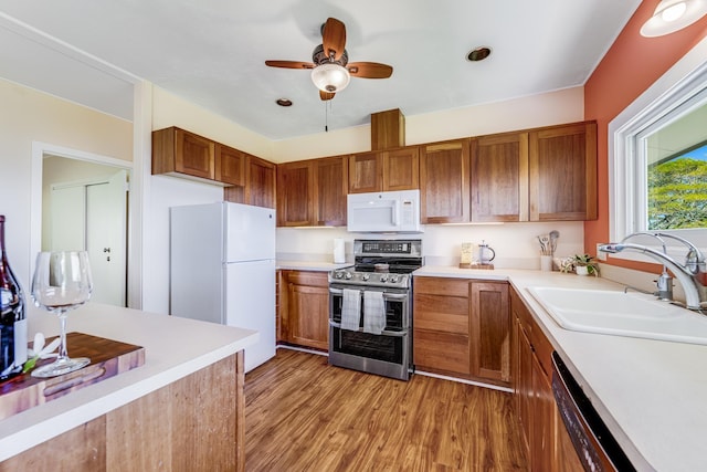 kitchen featuring light countertops, white appliances, brown cabinetry, and a sink