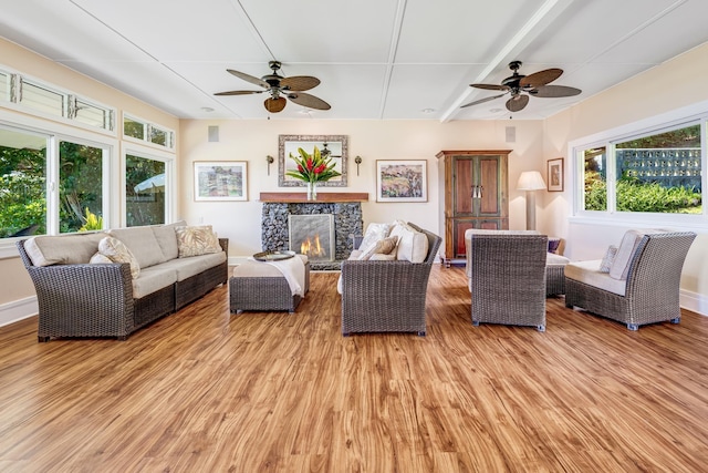 living room with a stone fireplace, wood finished floors, a ceiling fan, and baseboards