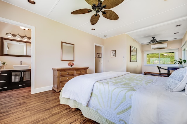 bedroom featuring baseboards, a wall unit AC, ceiling fan, wood finished floors, and a sink