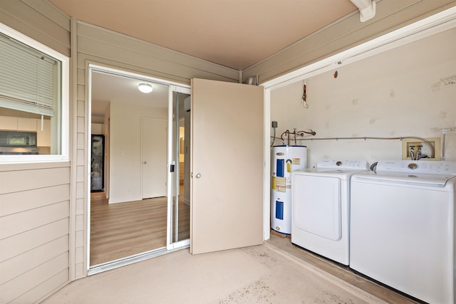 clothes washing area featuring water heater, washer and dryer, light hardwood / wood-style floors, and wood walls