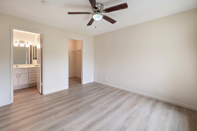 unfurnished bedroom featuring a walk in closet, connected bathroom, light wood-type flooring, and ceiling fan