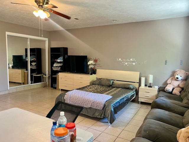 bedroom with ceiling fan, a closet, light tile patterned floors, and a textured ceiling