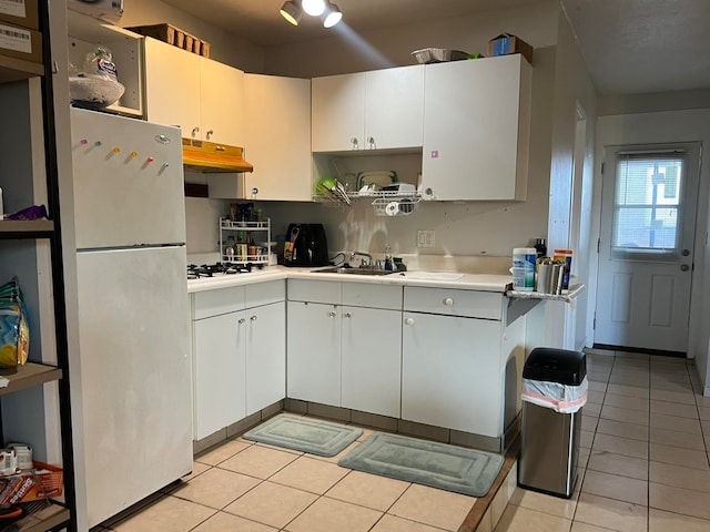 kitchen with light tile patterned flooring, white fridge, white cabinetry, and sink