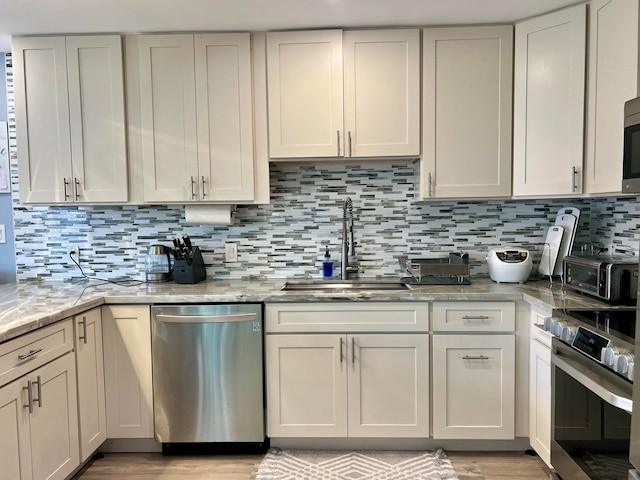 kitchen with sink, light stone countertops, appliances with stainless steel finishes, tasteful backsplash, and white cabinetry