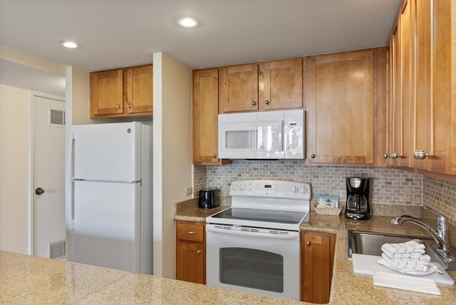 kitchen featuring visible vents, backsplash, brown cabinets, white appliances, and a sink