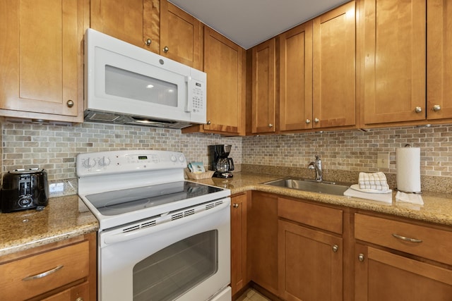 kitchen featuring brown cabinetry, backsplash, white appliances, and a sink