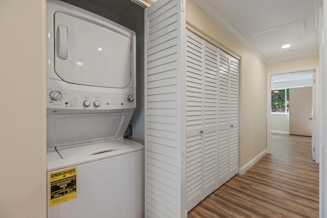 laundry room featuring dark hardwood / wood-style floors, stacked washer / dryer, and crown molding