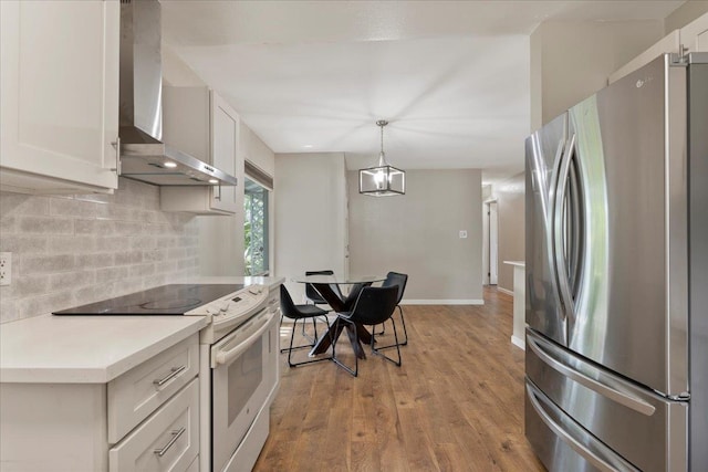 kitchen featuring hanging light fixtures, stainless steel fridge, light wood-type flooring, electric range, and wall chimney range hood