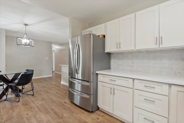 kitchen with white cabinetry, hanging light fixtures, light hardwood / wood-style flooring, stainless steel refrigerator, and tasteful backsplash