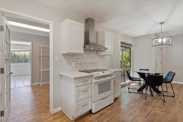 kitchen featuring light hardwood / wood-style flooring, white range, pendant lighting, wall chimney exhaust hood, and white cabinetry