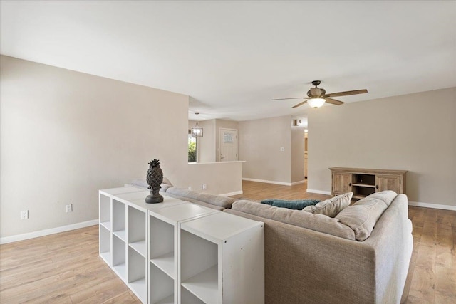 living room featuring ceiling fan with notable chandelier and light wood-type flooring