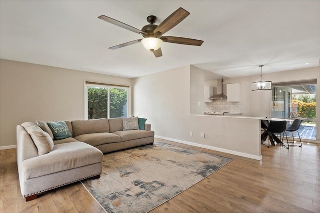 living room featuring a wealth of natural light, ceiling fan with notable chandelier, and light hardwood / wood-style flooring