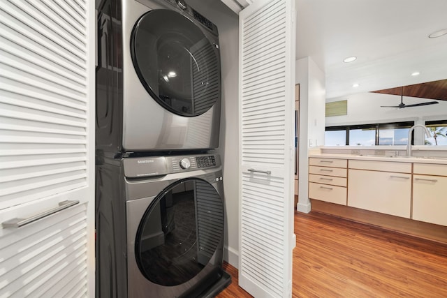 laundry area with sink, stacked washer / drying machine, light hardwood / wood-style flooring, and ceiling fan