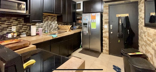 kitchen featuring dark brown cabinetry, sink, light tile patterned floors, stainless steel appliances, and decorative backsplash