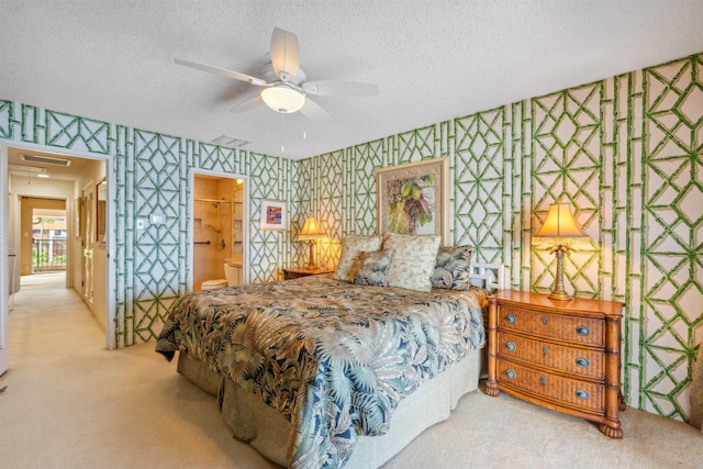 carpeted bedroom with a textured ceiling, ensuite bathroom, and ceiling fan