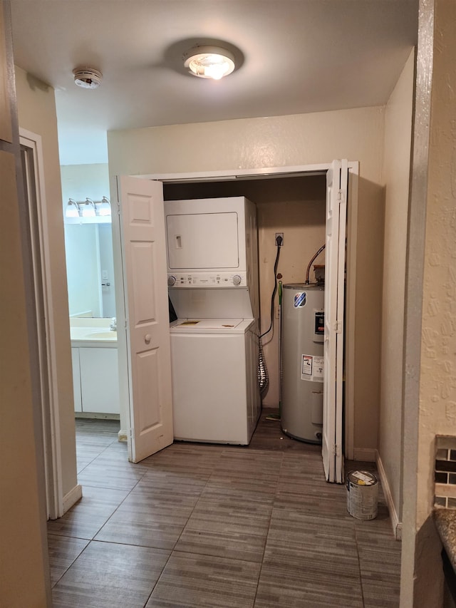 clothes washing area featuring water heater, sink, and stacked washer and clothes dryer