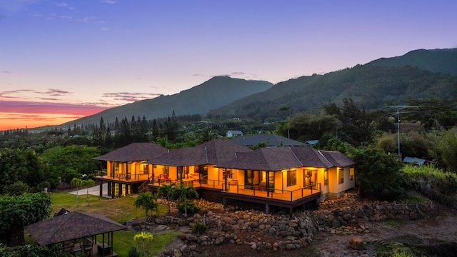 back house at dusk featuring a deck with mountain view, a gazebo, and a sunroom