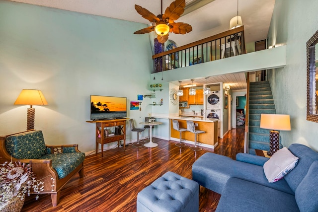 living room with ceiling fan, dark wood-type flooring, stacked washing maching and dryer, and a high ceiling