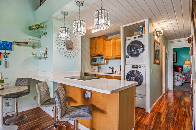 kitchen featuring kitchen peninsula, a kitchen breakfast bar, stacked washing maching and dryer, sink, and pendant lighting