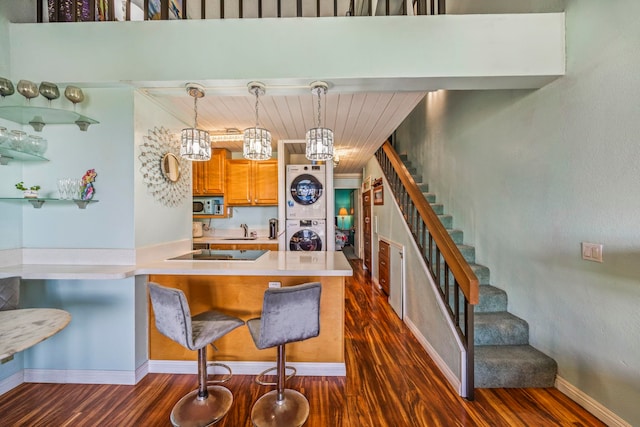 kitchen featuring kitchen peninsula, stacked washing maching and dryer, decorative light fixtures, a notable chandelier, and dark hardwood / wood-style floors