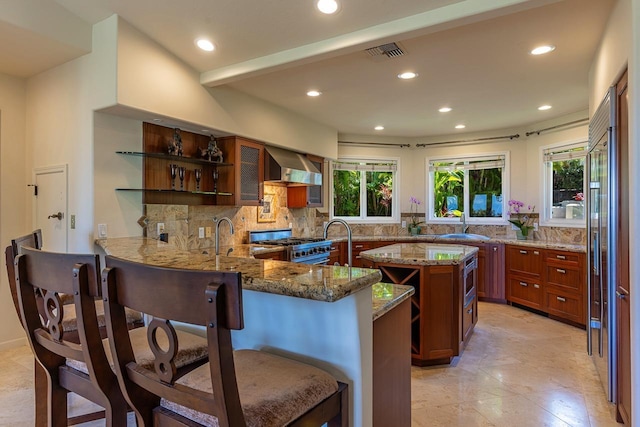 kitchen with wall chimney range hood, tasteful backsplash, open shelves, high end stainless steel range oven, and light stone countertops