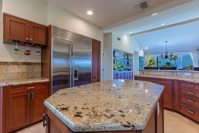 kitchen featuring brown cabinetry, lofted ceiling with beams, a center island, light stone countertops, and built in fridge