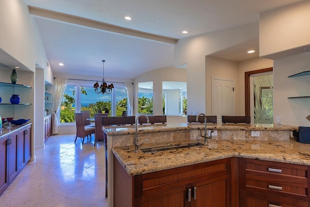 kitchen with a peninsula, an inviting chandelier, light stone counters, and a sink