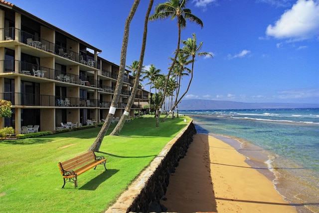 surrounding community with a yard, a water view, and a view of the beach