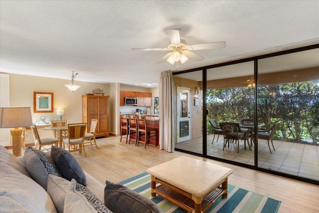 living room with a textured ceiling, a wall of windows, ceiling fan, and light wood-type flooring