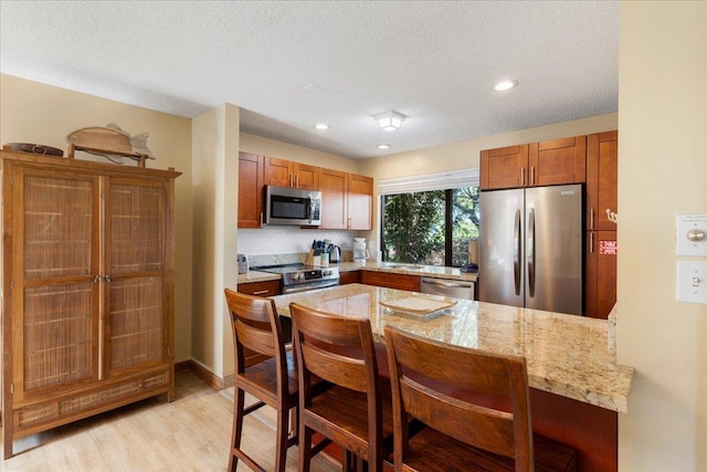 kitchen featuring a breakfast bar area, appliances with stainless steel finishes, backsplash, light stone countertops, and kitchen peninsula