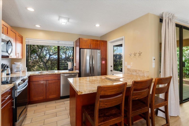 kitchen featuring appliances with stainless steel finishes, sink, a breakfast bar area, light stone counters, and kitchen peninsula