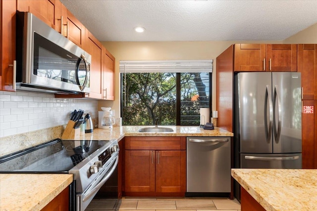 kitchen featuring sink, stainless steel appliances, light stone counters, a textured ceiling, and decorative backsplash