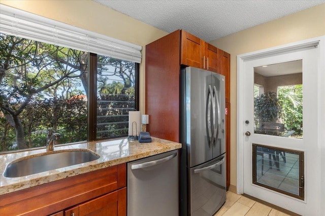 kitchen featuring light stone countertops, appliances with stainless steel finishes, sink, and a textured ceiling