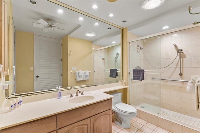 bathroom with a shower with door, ceiling fan, tile patterned flooring, vanity, and toilet