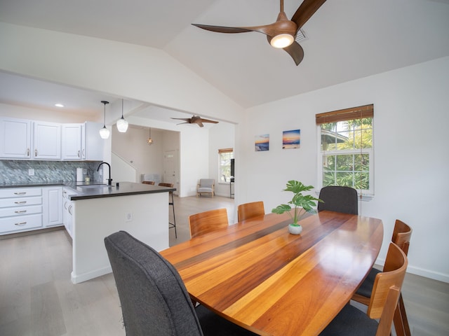 dining space featuring ceiling fan, sink, light wood-type flooring, and vaulted ceiling