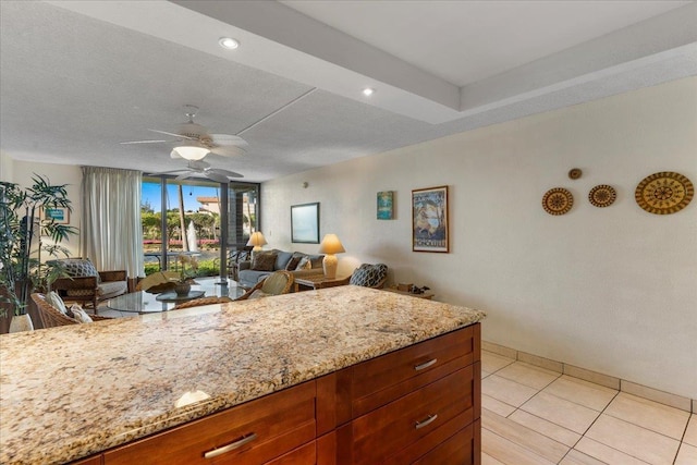kitchen with a ceiling fan, open floor plan, light stone counters, and light tile patterned flooring
