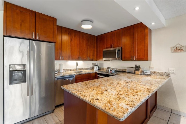 kitchen with light tile patterned flooring, light stone counters, a sink, stainless steel appliances, and a peninsula