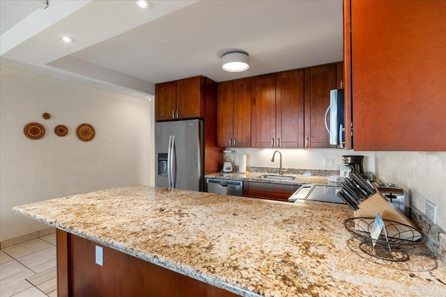 kitchen with a peninsula, light stone countertops, appliances with stainless steel finishes, and a sink